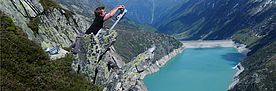 Ein Forscher lehnt auf einem Felsblock hoch über einem Stausee und bedient ein Messgerät.